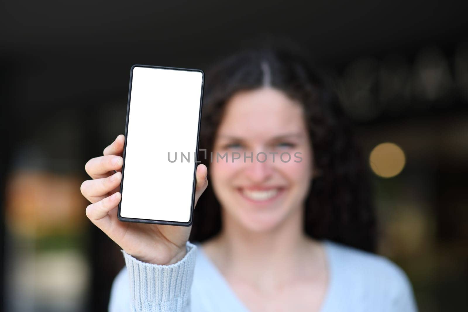 Front view of a happy woman showing at camera blank phone