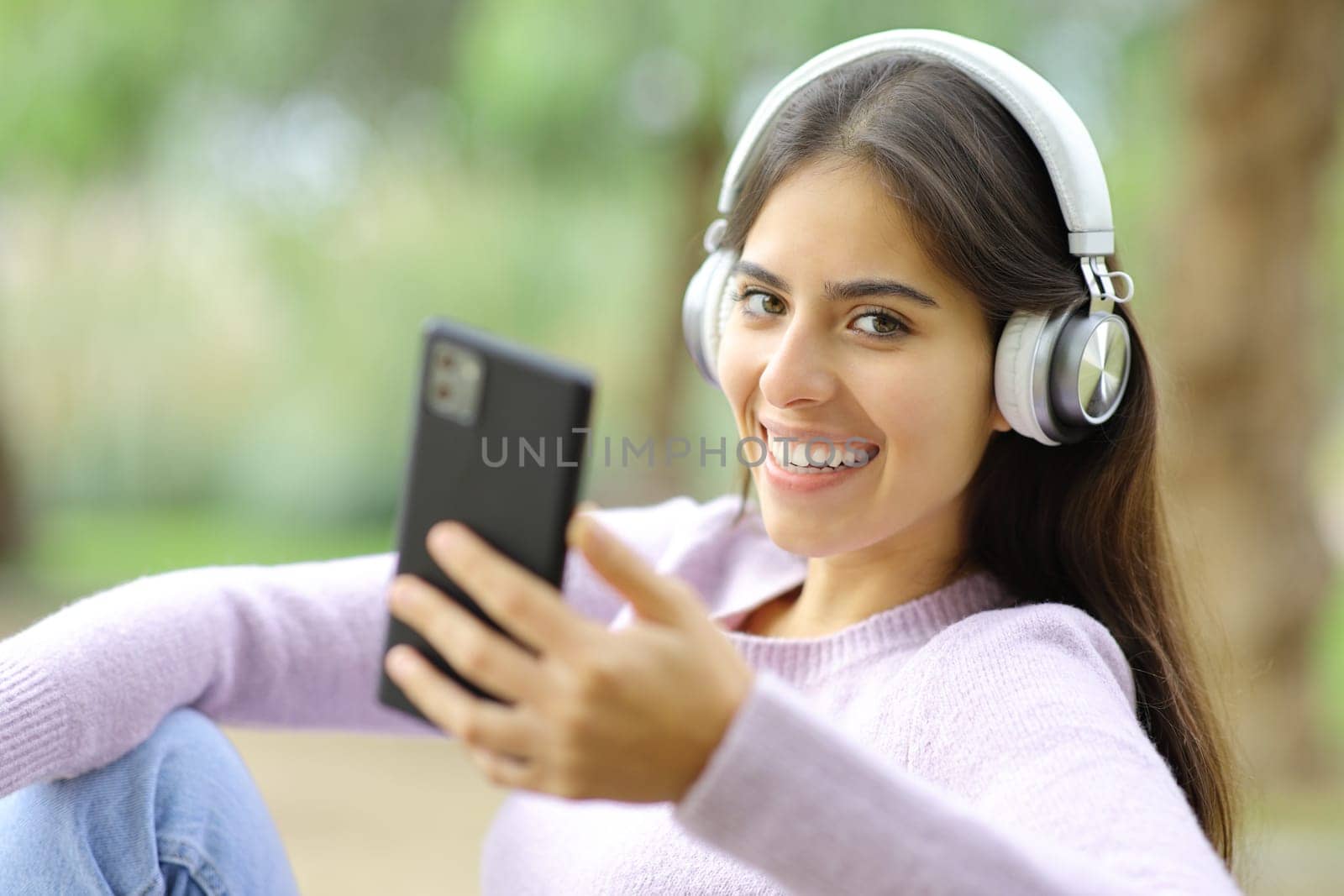 Happy woman listening to music looking at camera in a park