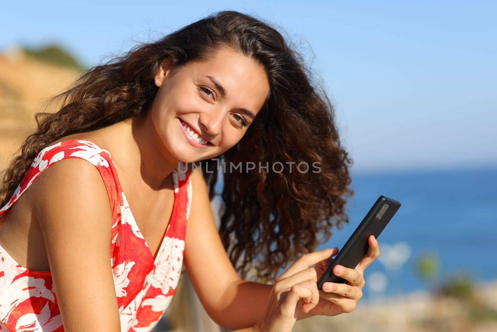 Happy tourist on the beach looks at camera holding phone
