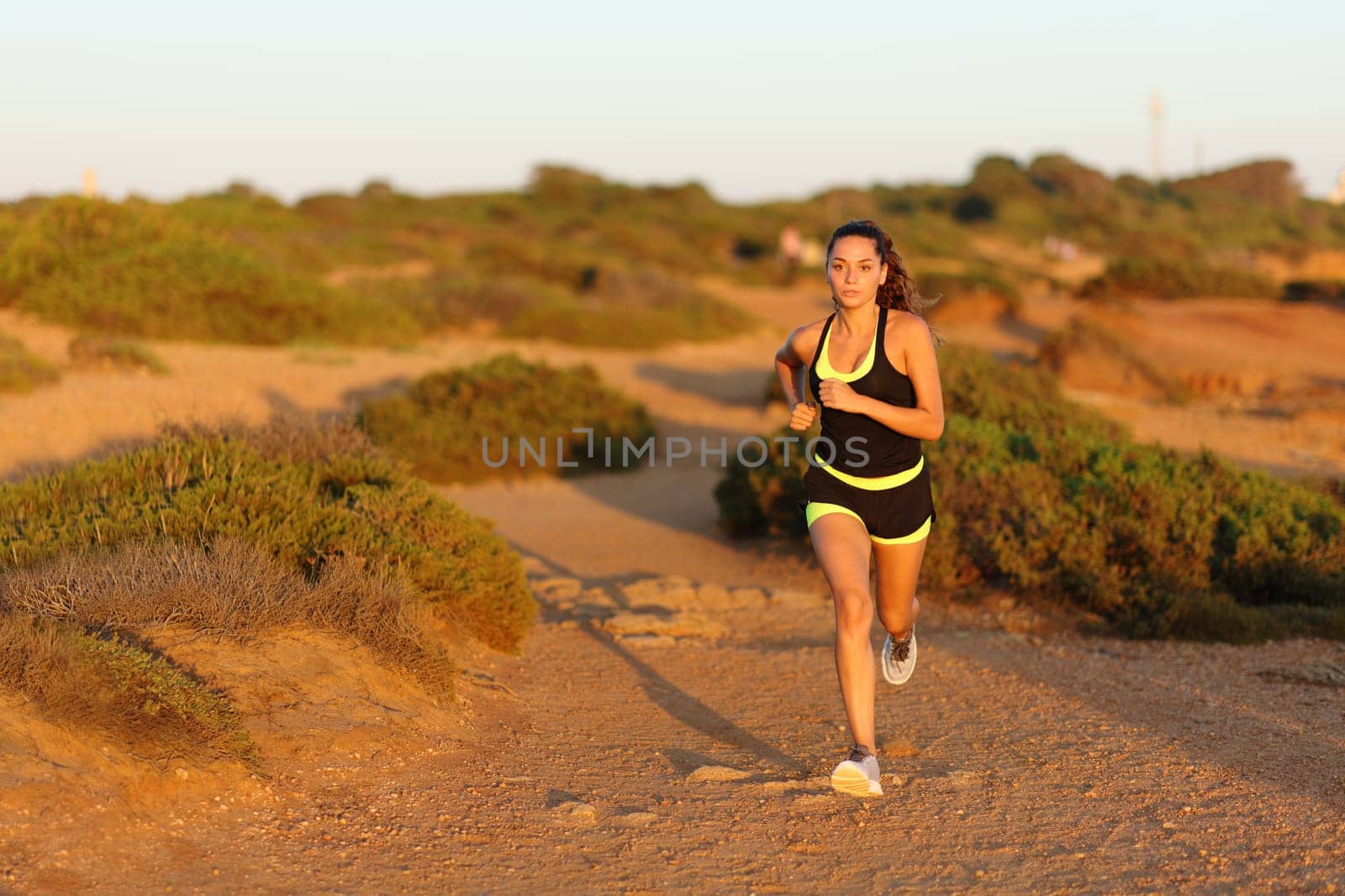 Front vie wof a runner woman running in the mountain towards camera at sunset