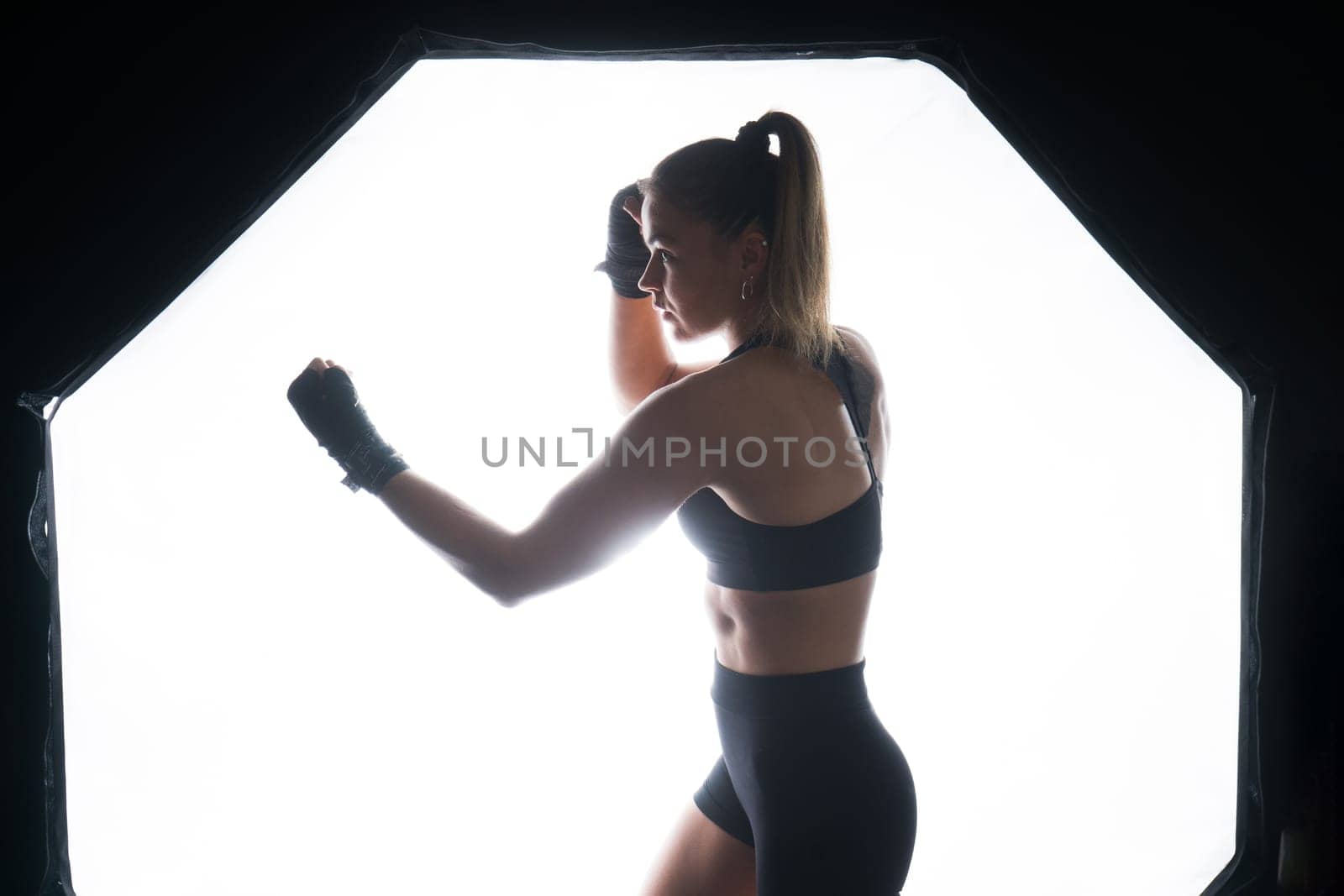 Cool female fighter in boxing bandages trains in a studio. Mixed martial arts.