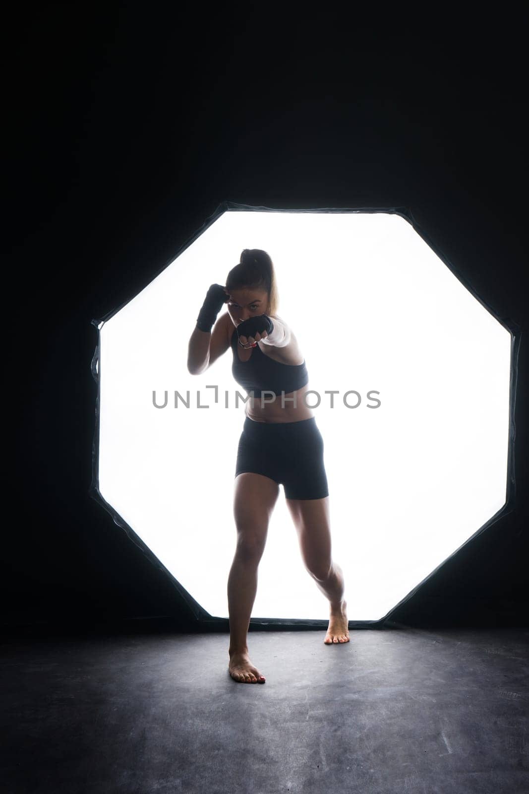 Cool female fighter in boxing bandages trains in a studio. Mixed martial arts.