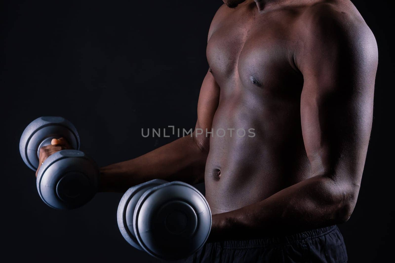 Isolated african muscular man with dumbbells on a dark studio background. Strong shirtless black guy