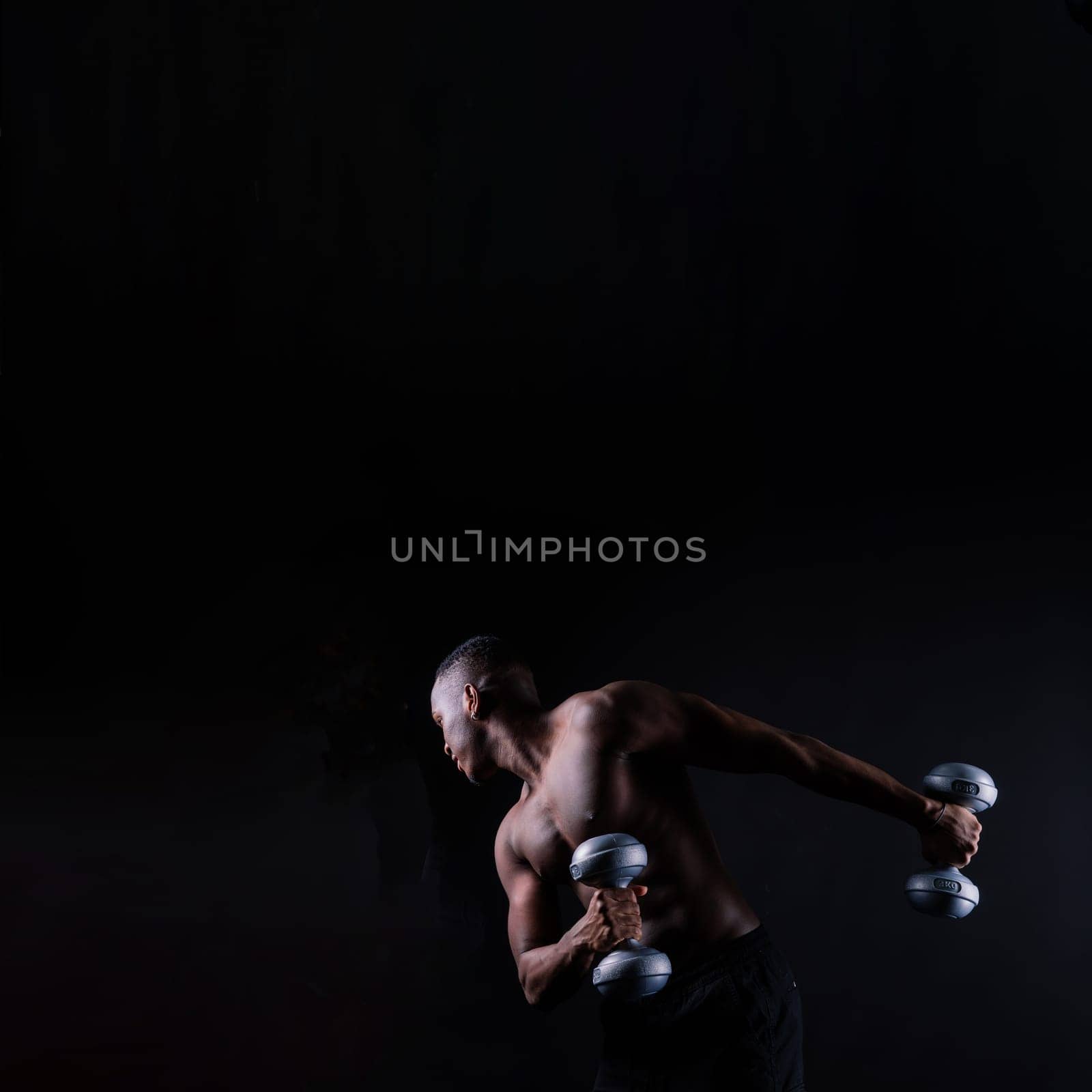 Isolated african muscular man with dumbbells on a dark studio background. Strong shirtless black guy
