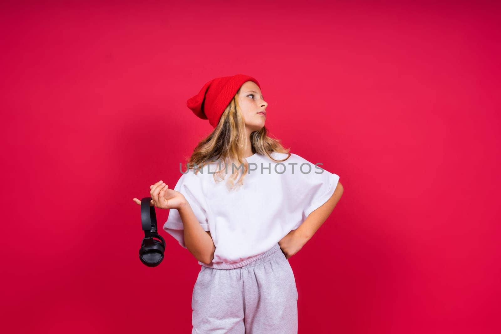 Girl listening to music in headphones on a red background. Cute child enjoying dance music, smile