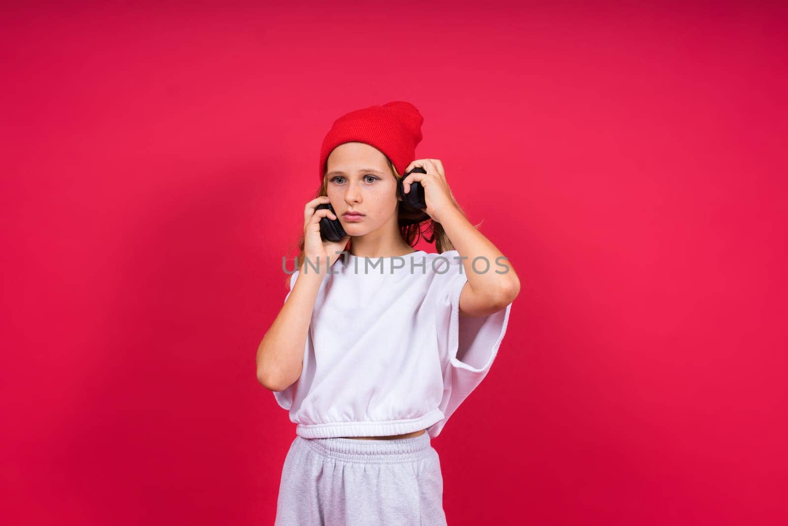 Girl listening to music in headphones on a red background. Cute child enjoying dance music, smile
