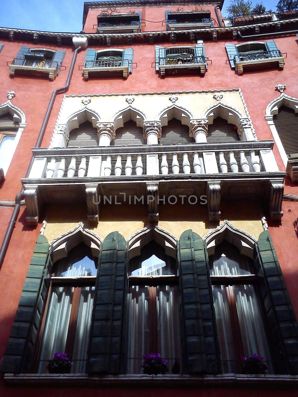 Venice, Italy. May 30, 2020. Facade of a beautiful Venetian building. The palace has pink walls, many windows and wooden shutters. View from below. A masterpiece of Venetian architecture. Journey to Italy