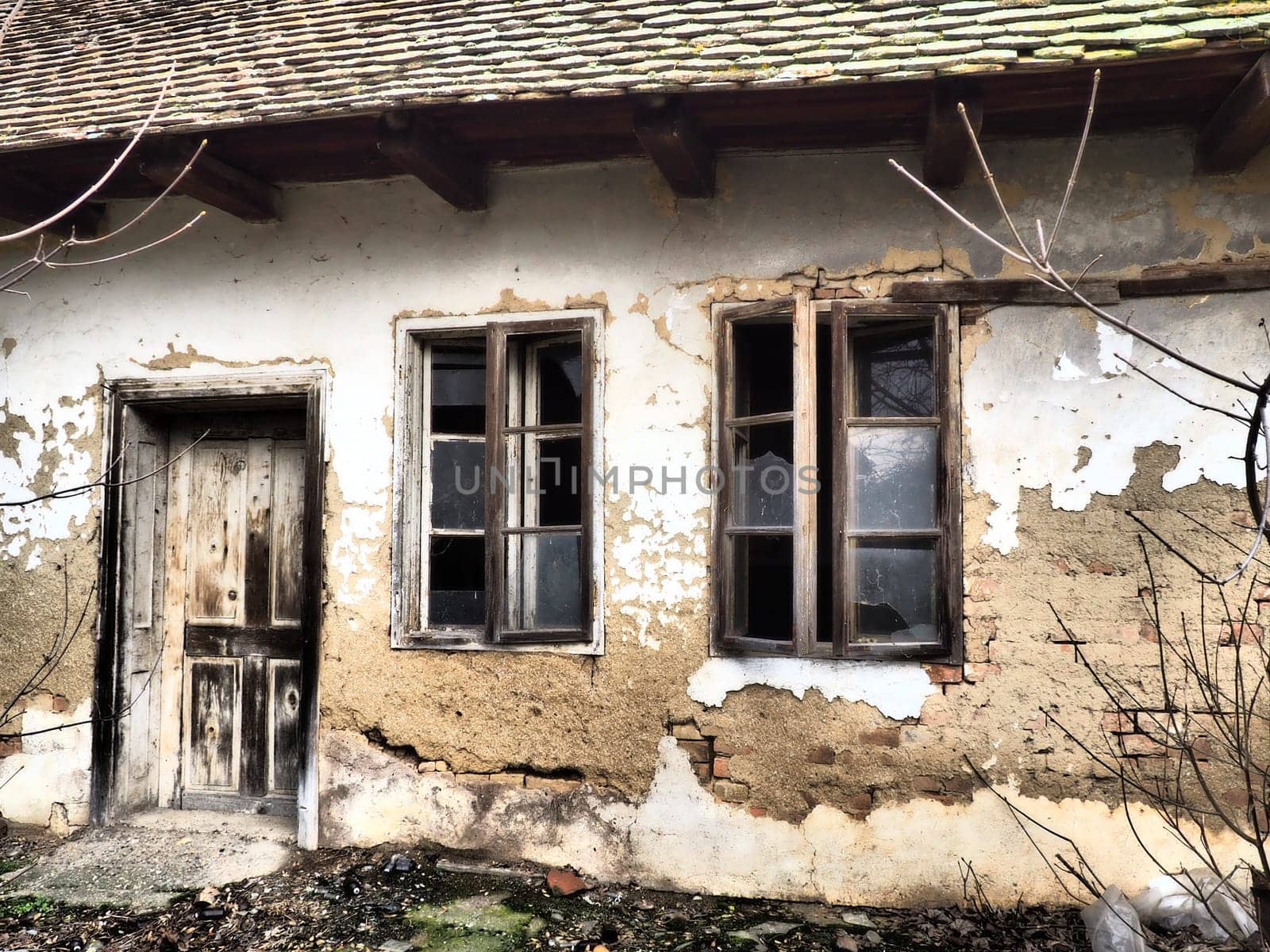 Old house with windows and a door. Collapsing rural house. The concept of urbanization and oblivion of the motherland. Abandoned house. Broken glass in the window and falling plaster. Serbia. Balkans.