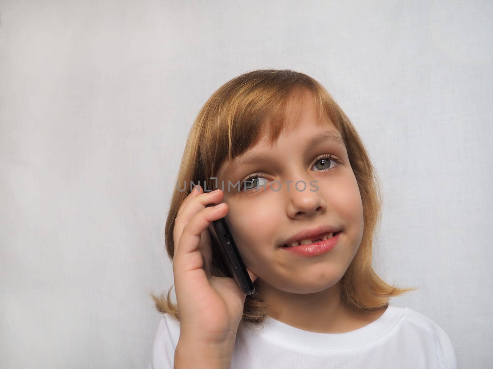 7-year-old girl with no front tooth. The child smiles, looks away and listens to someone on the phone or smartphone. Change of milk teeth in childhood. Modern communication technologies.