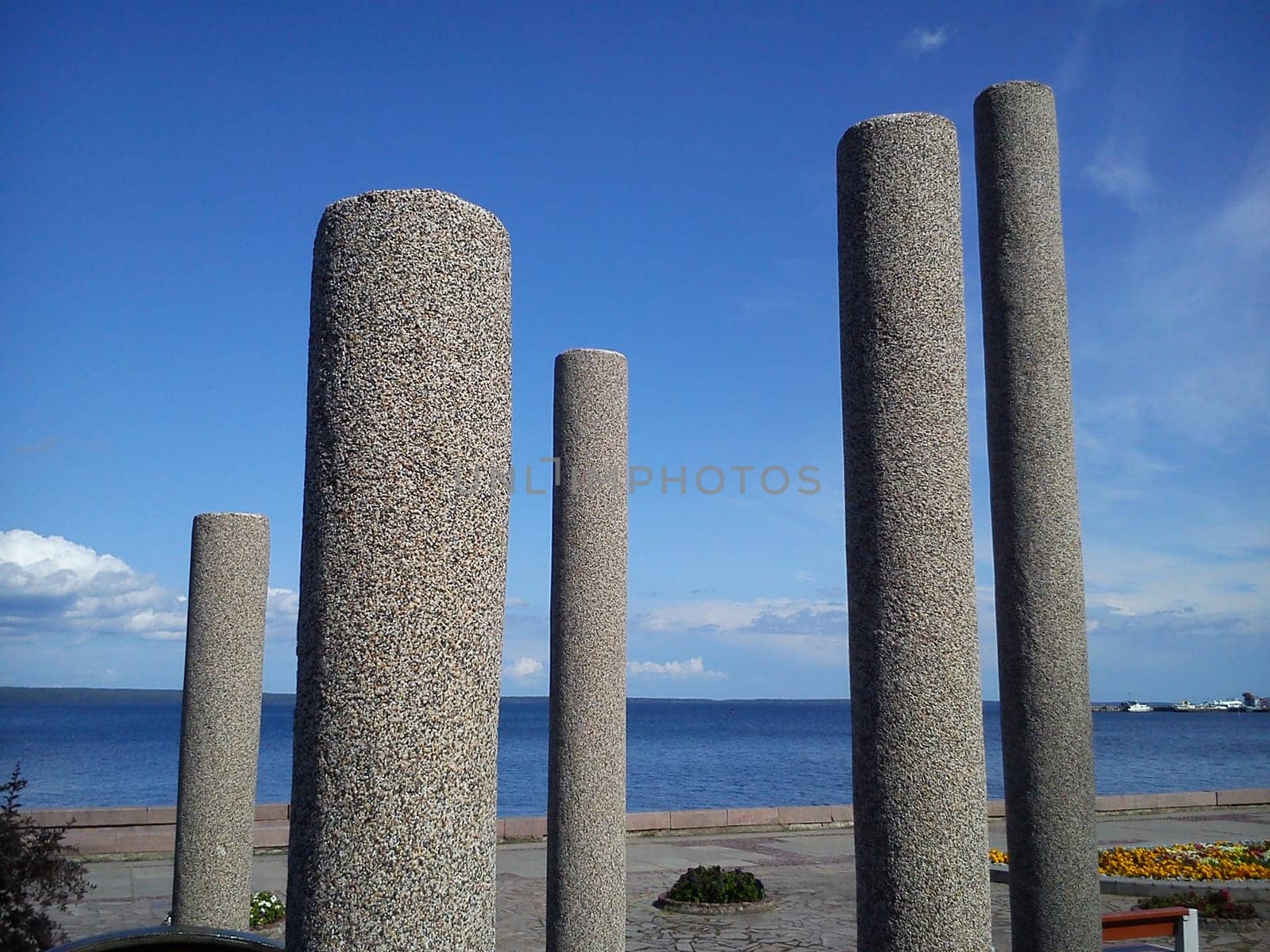 gray concrete pillars on the embankment of the lake, and in the background - blue sky and clouds
