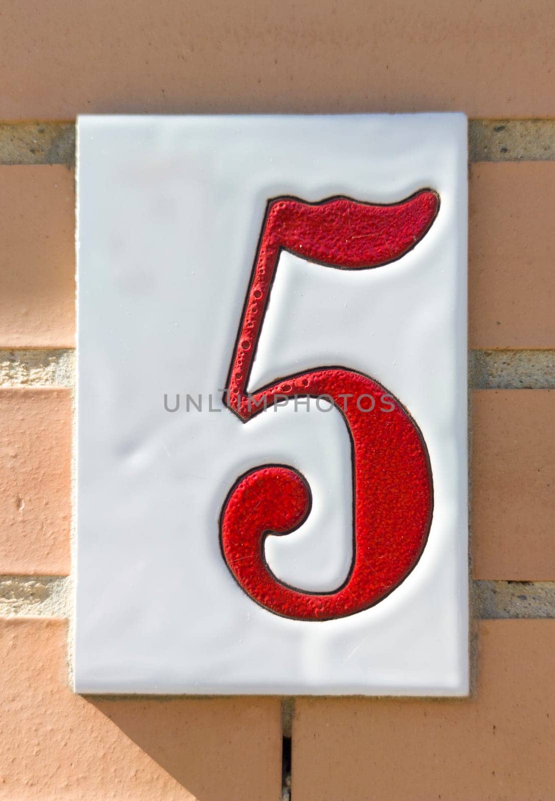 House number 5 over brick sunny wall. Houses with personality concept