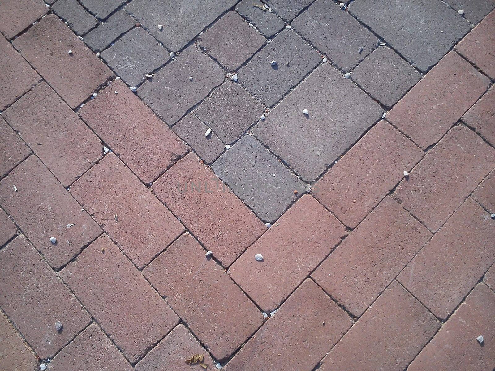 Burgundy and gray street paving tiles with small white pebbles. Rectangular decorative tile on the road. Rough edges of concrete. Tiles laid diagonally.