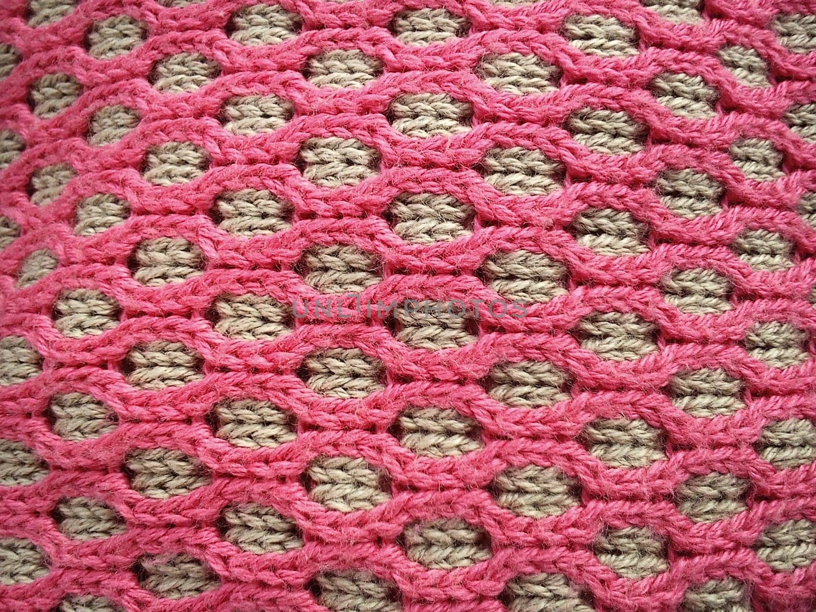 Close-up of decorative knitting. Machine or neat hand-knitted thing. The basis is beige yarn, the outer ornament is pink threads of the same thickness. Smooth hinges. Ovals or honeycombs as a pattern
