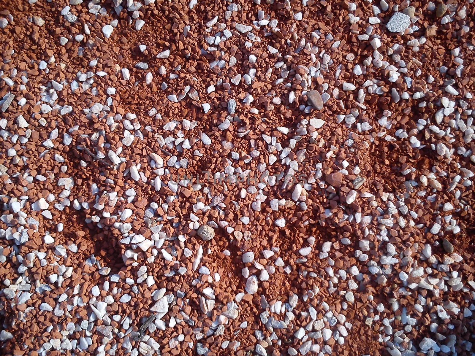 Fine decorative color granite crushed stone. Red-brown colored stone chips are used for landscaping. Crushed marble, granite, gravel or sand. Spots of fine white pebbles on heterogeneous soil.