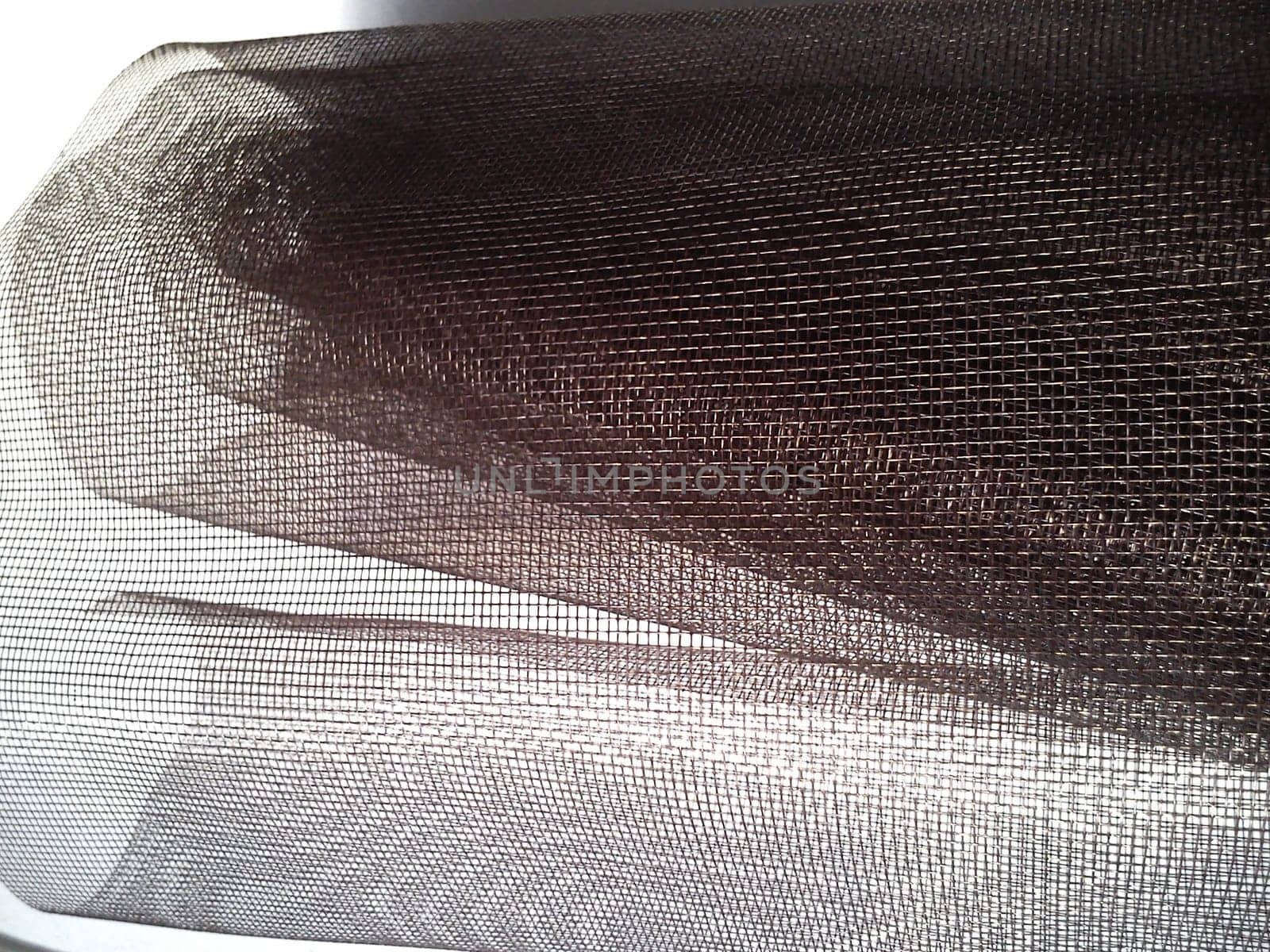 Mosquito net in a roll. Brown synthetic material on a white background. Weaving plastic threads. Convoluted lattice
