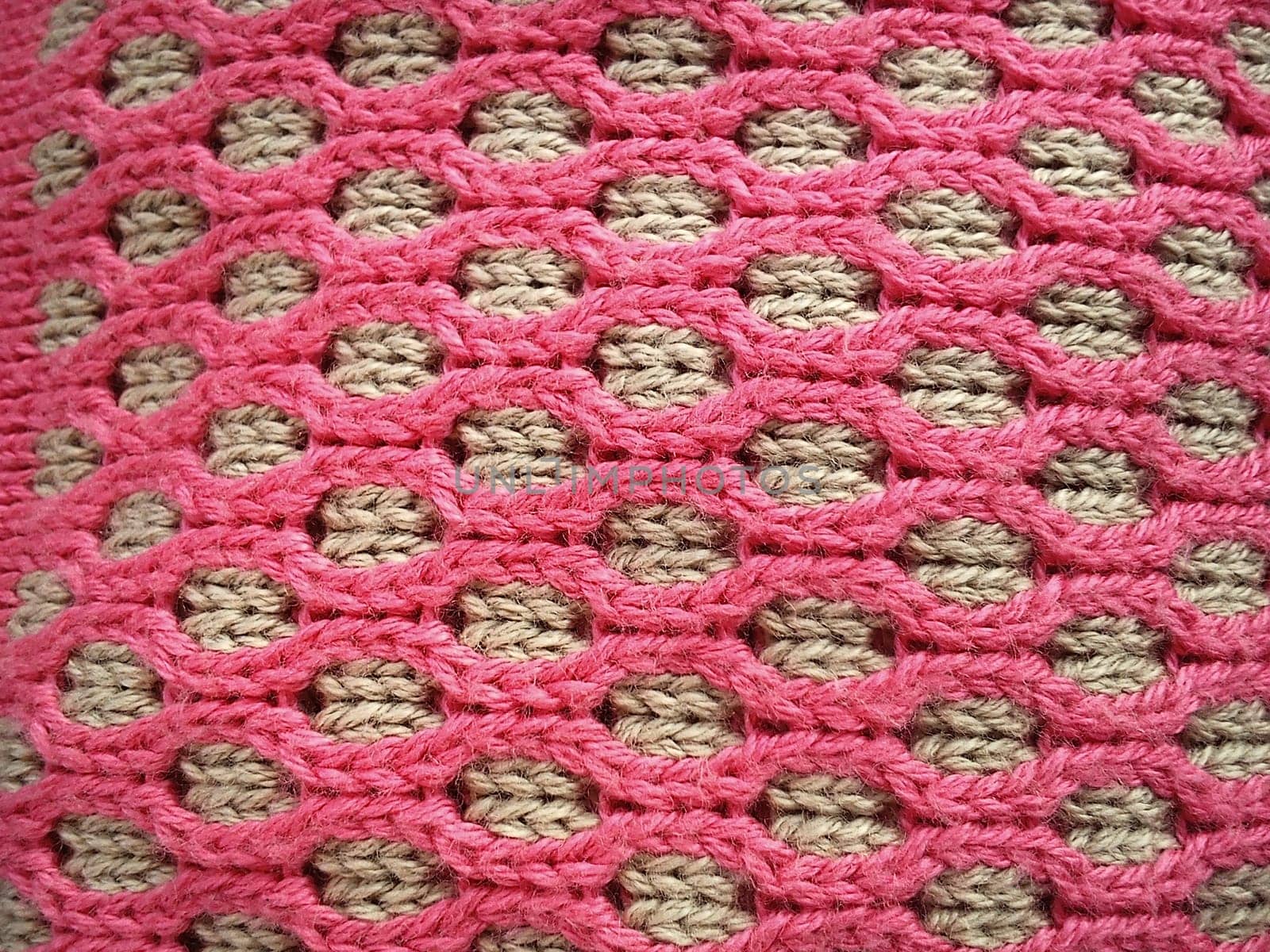 Close-up of decorative knitting. Machine or neat hand-knitted thing. The basis is beige yarn, the outer ornament is pink threads of the same thickness. Smooth hinges. Ovals or honeycombs as a pattern