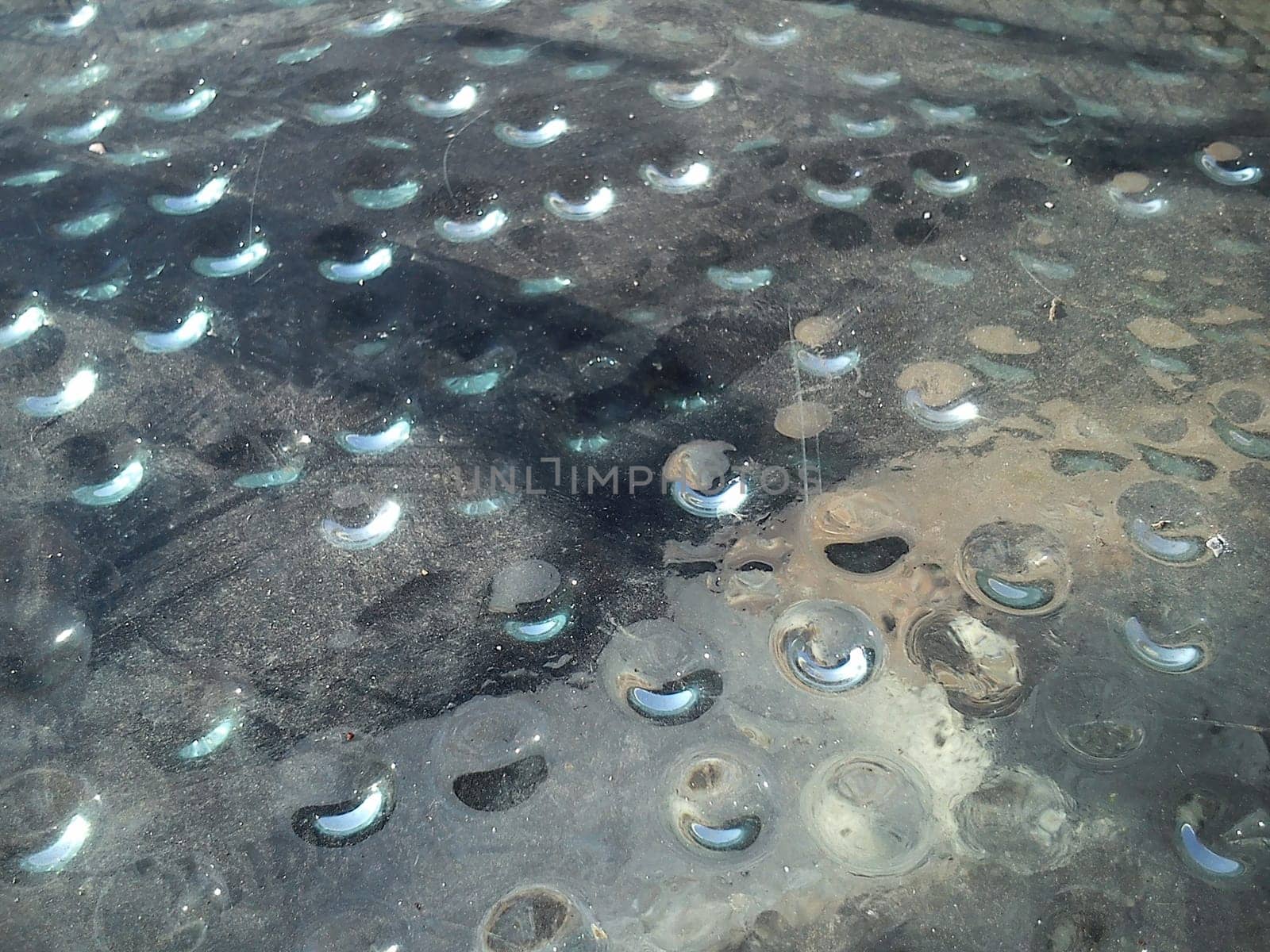 Condensed water in the form of hanging drops, photographed from above. Drops gathered under a stack covering an ancient Roman excavation. Dust on the glass. Rays of the sun under glass