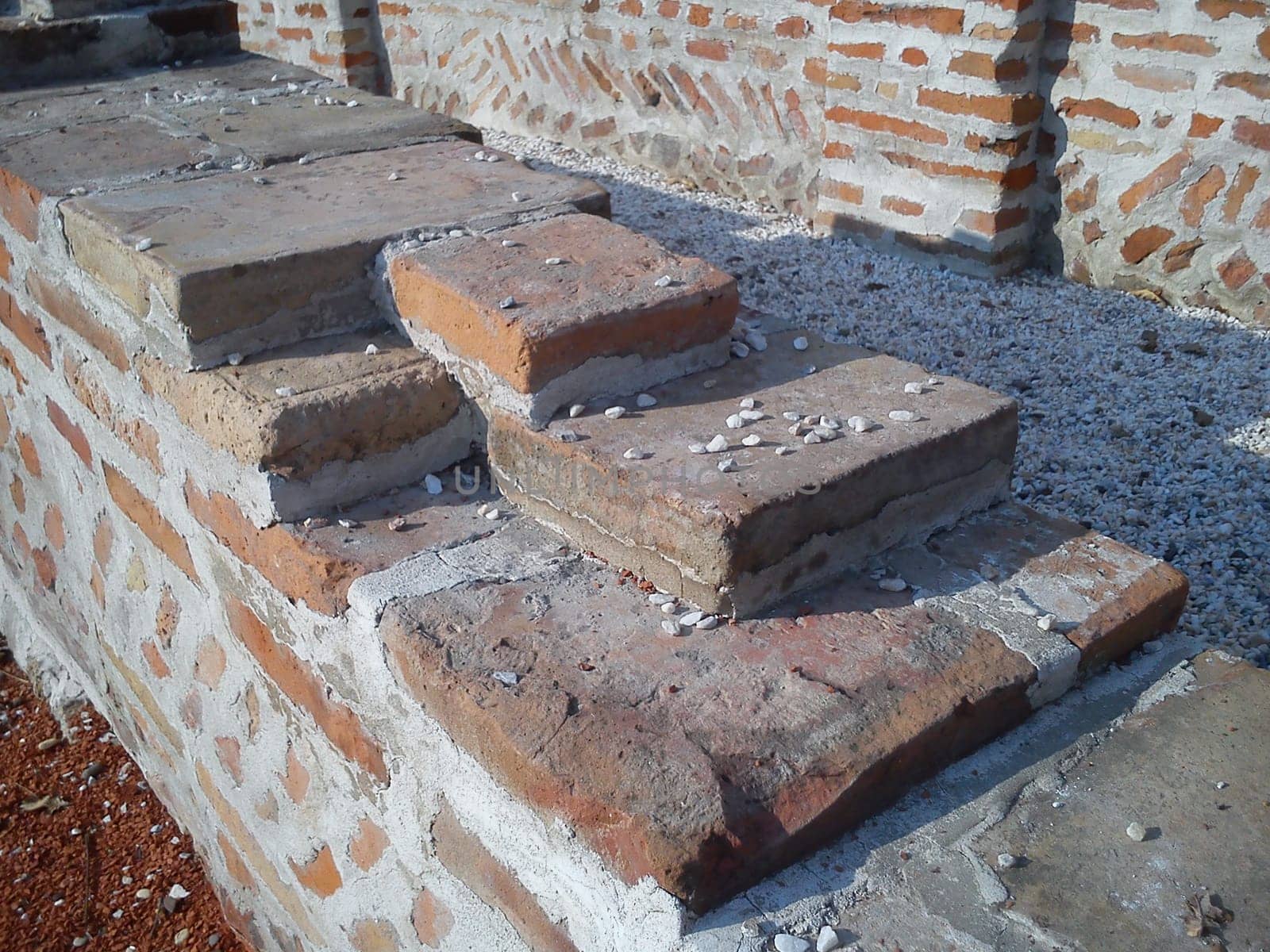 Old roman brick. The restored wall of the building of Roman times. Sunlight accentuates the warm brown-red shades of uneven bricks. Archaeological excavations of steps and walls of ancient buildings.