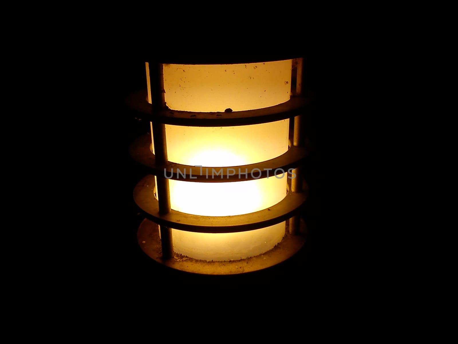 Street lamp turned on in a city park. Frosted opaque glass with a dull, warm, yellow light. A metal rim or cage into which a glass bulb is placed. Small insects strive for light.