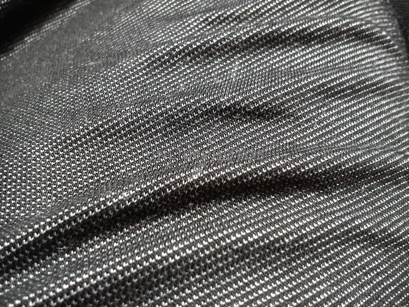Textile fabric made on a loom by weaving mutually perpendicular yarns. Gray synthetic fabric for sewing clothes, upholstery and other products. Material close-up. Crumpled waves on the fabric.