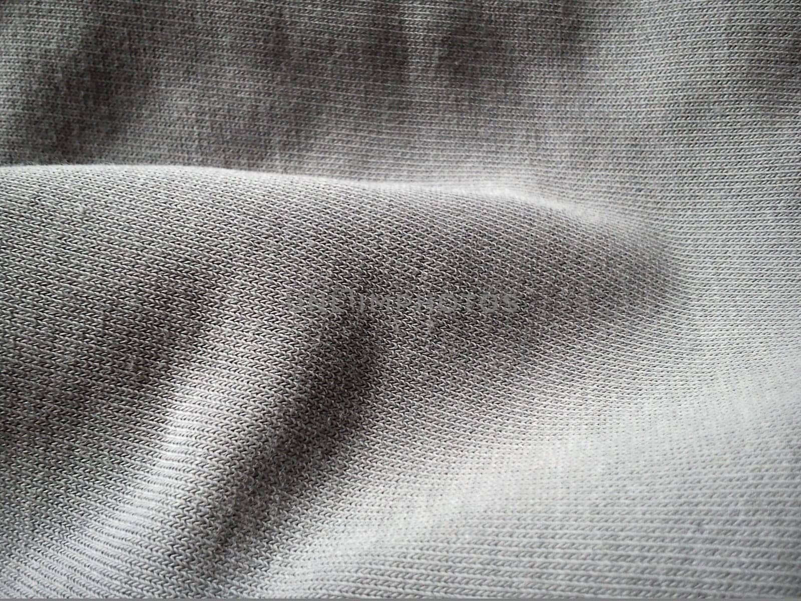 texture of a gray knitted fabric, slightly folded in waves or wrinkled. The play of light and shadow on a machine-knitted fabric in natural daylight. Soft, thick cotton material.