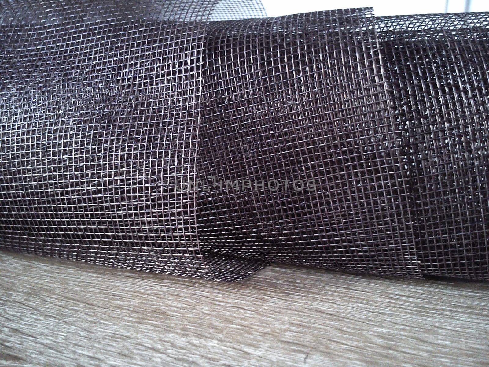 Mosquito net in a roll. Brown synthetic material on a white background. Weaving plastic threads. Convoluted lattice