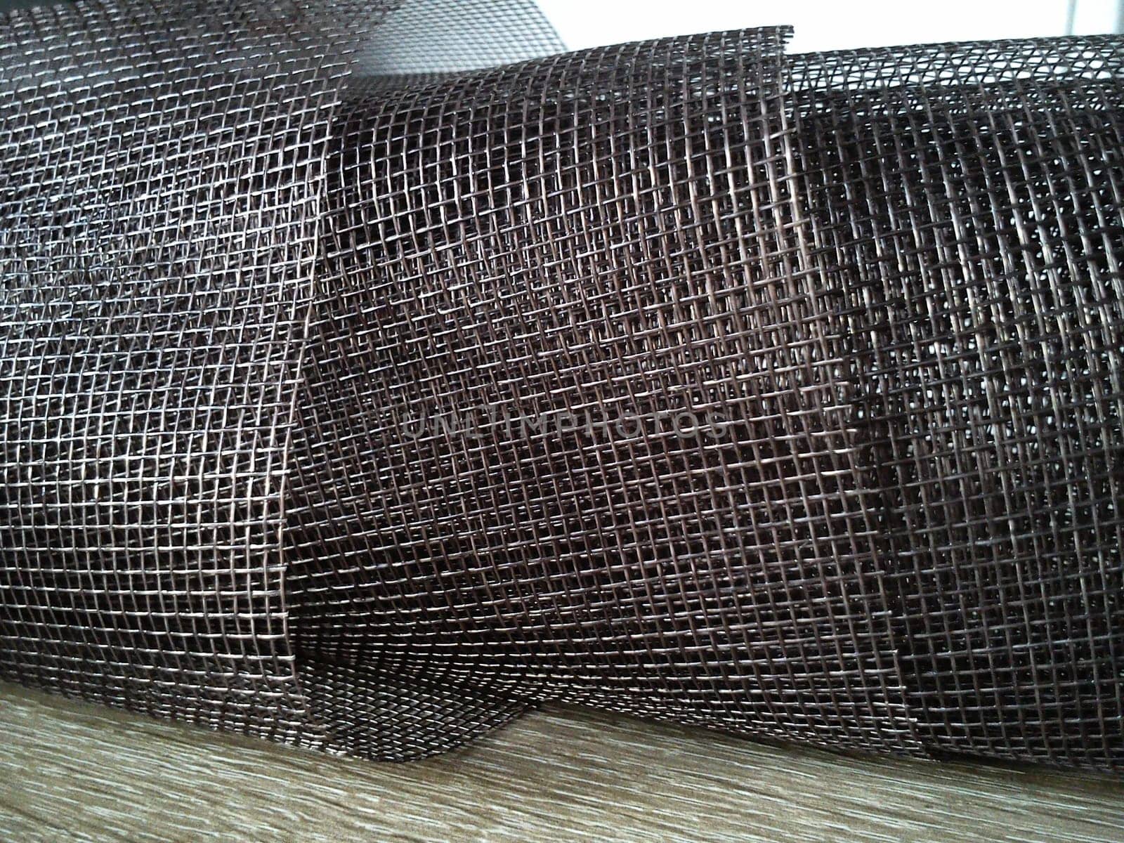 Mosquito net in a roll. Brown synthetic material on a white background. Weaving plastic threads. Convoluted lattice