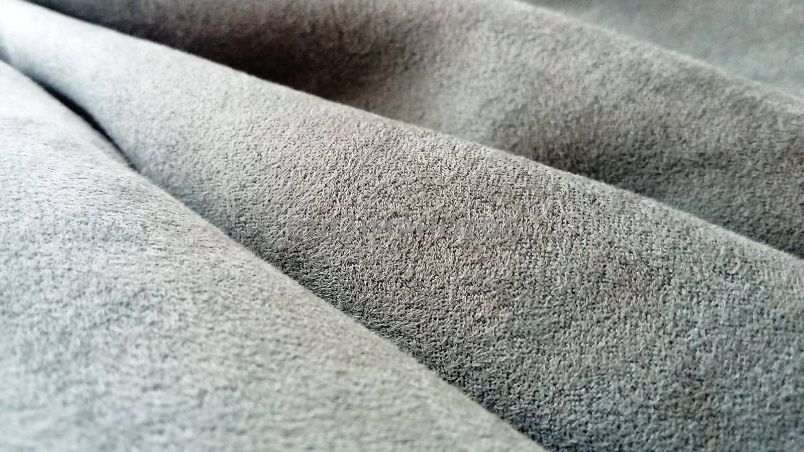 A close-up of velvety dense fabric for curtains of gray color, randomly folded by beautiful smooth waves. Natural daylight