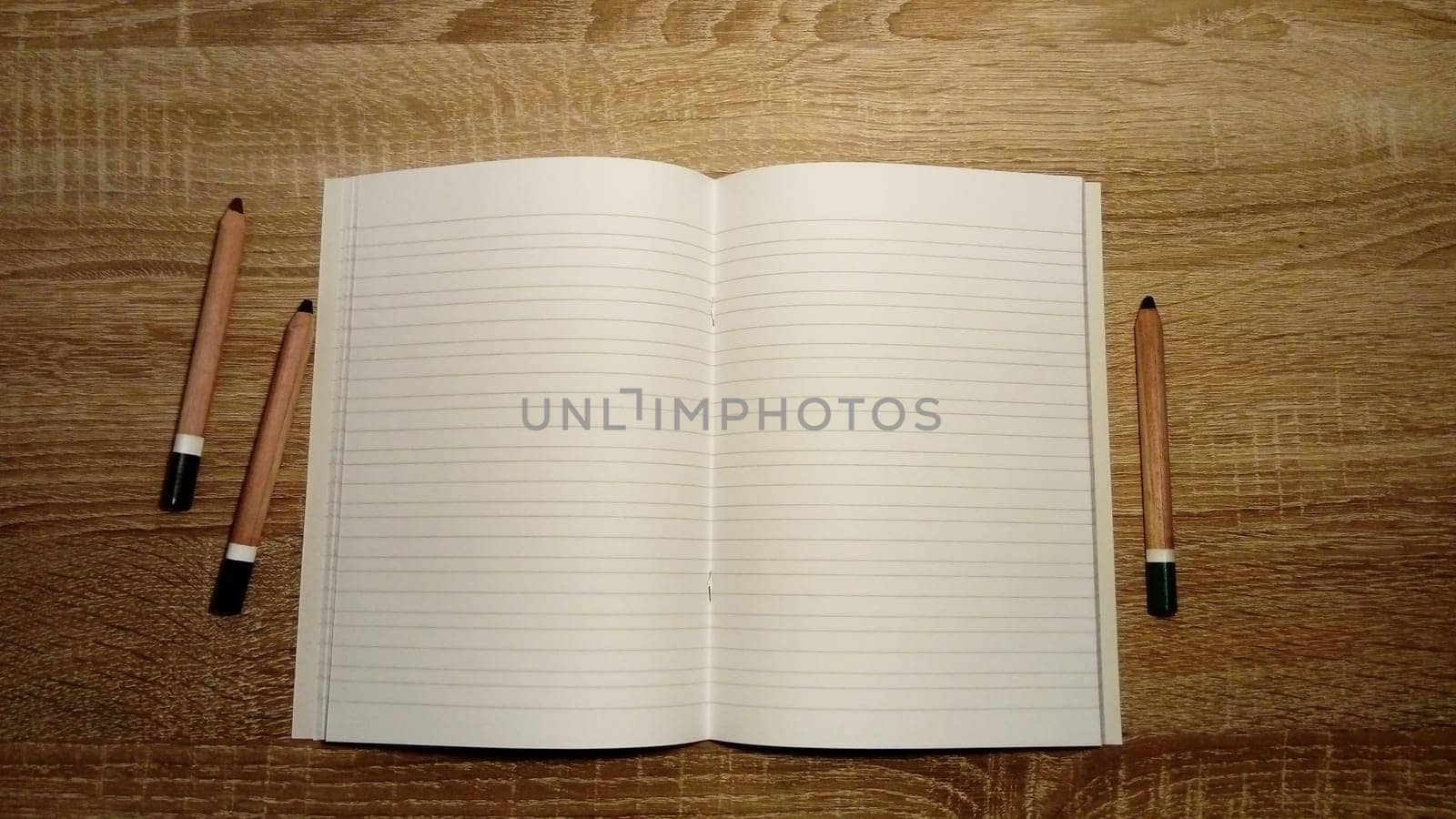 U-turn notebook with blank white pages. To the left and right of the notebook on the wooden table are colored pencils.
