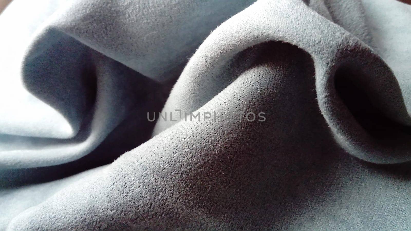 A close-up of a velvety dense fabric for curtains of gray-blue color, randomly folded by beautiful smooth waves with a play of light and shadow. Natural daylight