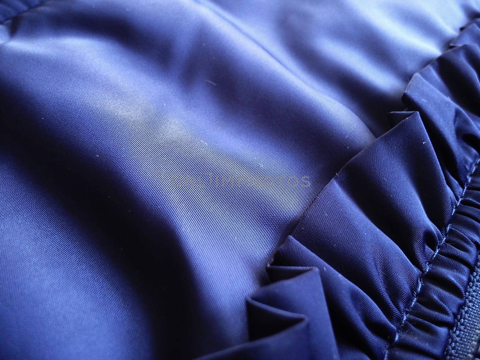 A fragment of a garment made of synthetic polyester fabric. The play of light and shadow on blue material. Right - sewn decorative element in the form of a shuttlecock.