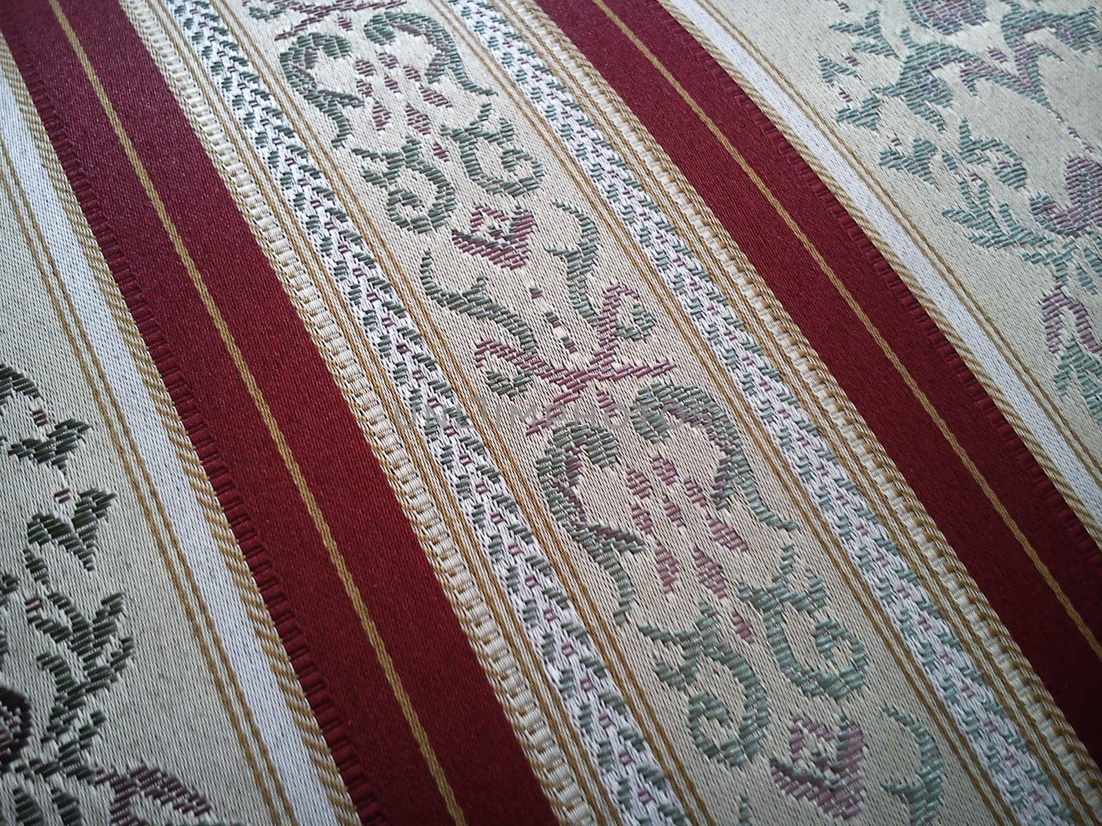 A sample of dense fabric for upholstery of upholstered furniture. The pattern of floral and floral elements in beige shades is combined with wide dark red stripes
