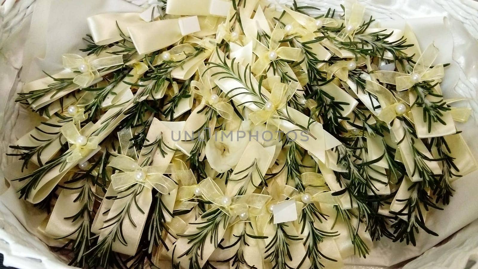 A few twigs of rosemary pinned to the festive wedding bows. The jewelry lies in a basket on a silk decorative pillow. Used as a decoration for guests at a wedding.