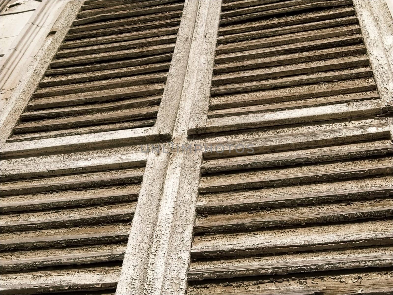 Old wooden shutters on the window. Antique wooden architecture. Dry wood with rustling discolored paint. Husk and dust. Natural color. Window sill, horizontal stripes and slats.