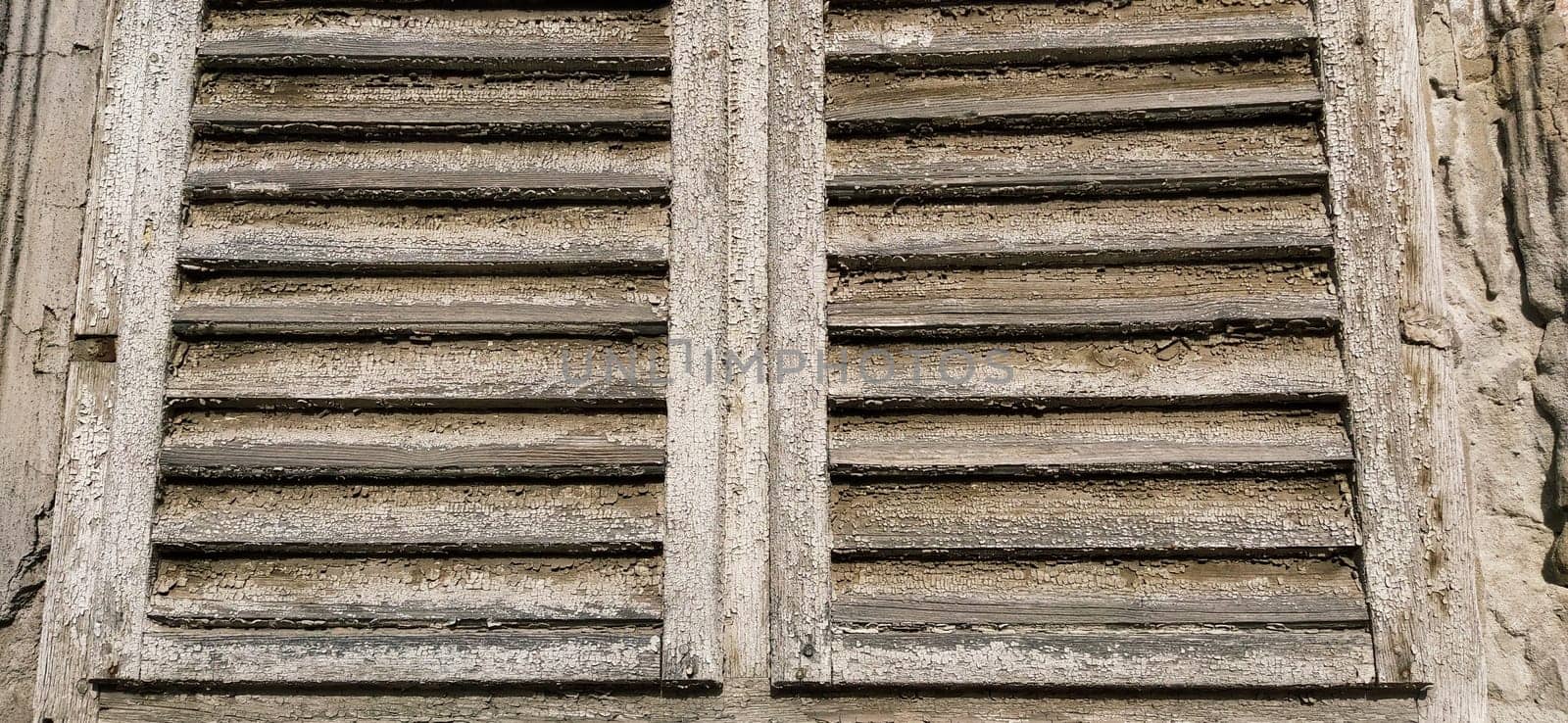 Old wooden shutters on the window. Antique wooden architecture. Dry wood with rustling discolored paint. Husk and dust. Natural color. Window sill, horizontal stripes and slats