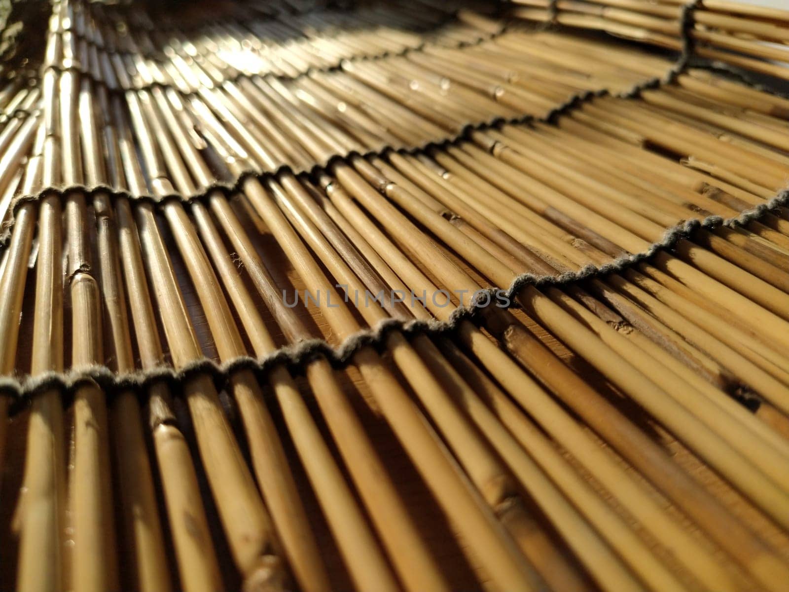A straw bedding, tablecloth or small rug laid on a table and photographed from the side. Soft evening sunlight reflects off the stems. Some sticks are broken, threads and ropes are braided.