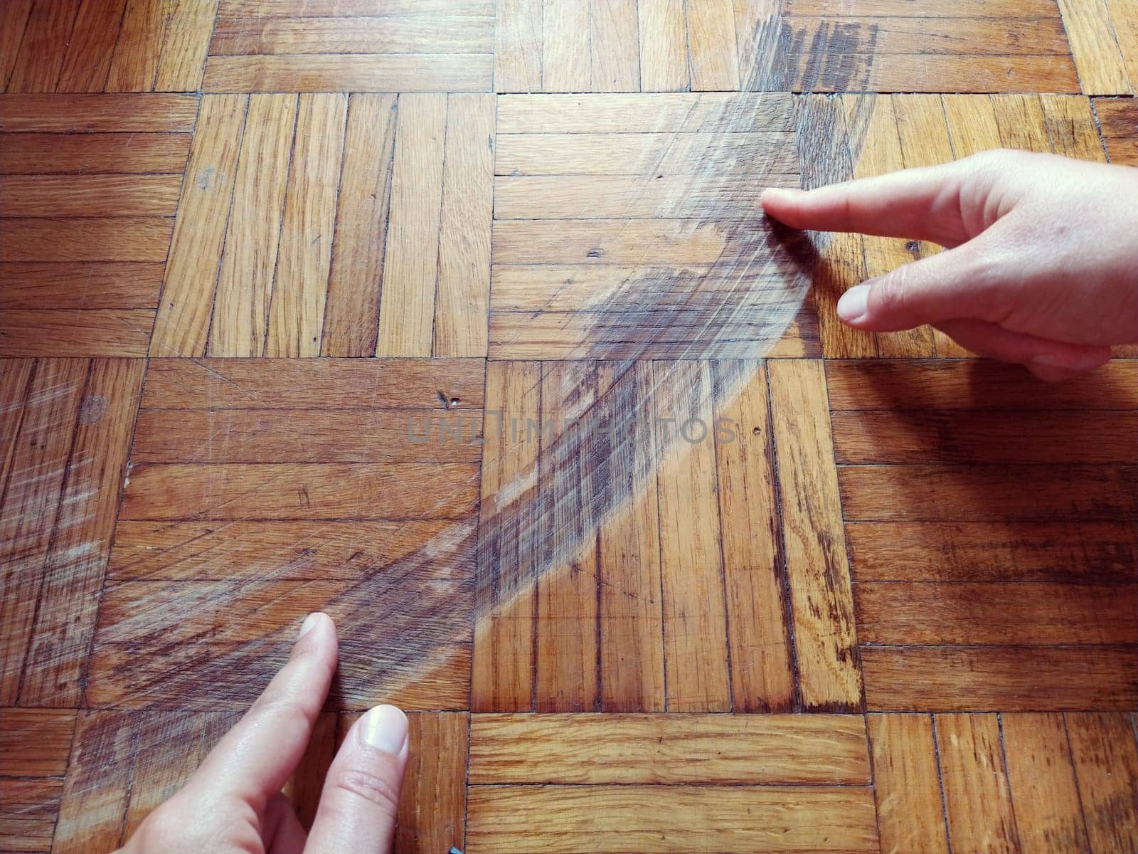 Old, scratched parquet flooring needs maintenance. the parquet is damaged by scratches from prolonged use. Master's hands show damage to the floor