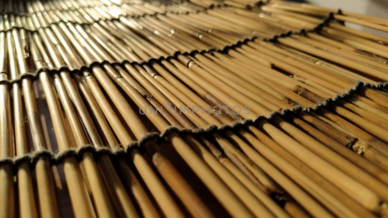 A straw bedding, tablecloth or small rug laid on a table and photographed from the side. Soft evening sunlight reflects off the stems. Some sticks are broken, threads and ropes are braided.
