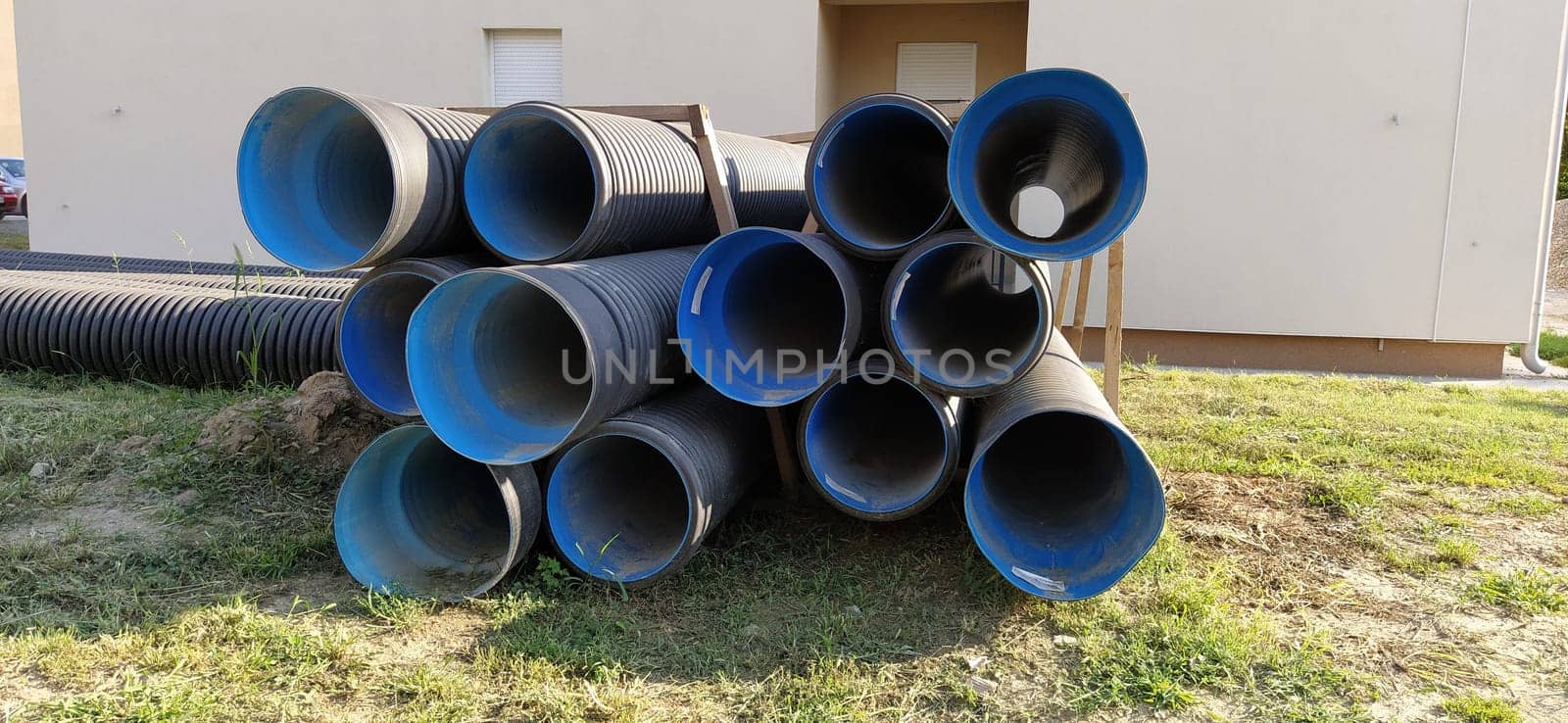 Sremska Mitrovica, Serbia, 23 August 2020. Metal corrugated pipes, blue inside. Plumbing or heating pipes lie on the ground next to a residential building. Corrugated metal. Production of technical and construction pipes