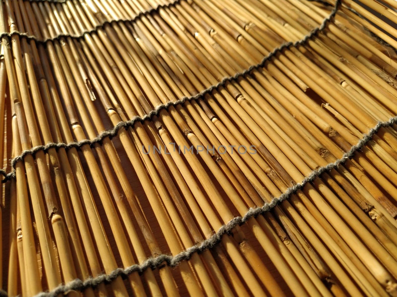 A straw bedding, tablecloth or small rug laid on a table and photographed from the side. Soft evening sunlight reflects off the stems. Some sticks are broken, threads and ropes are braided.