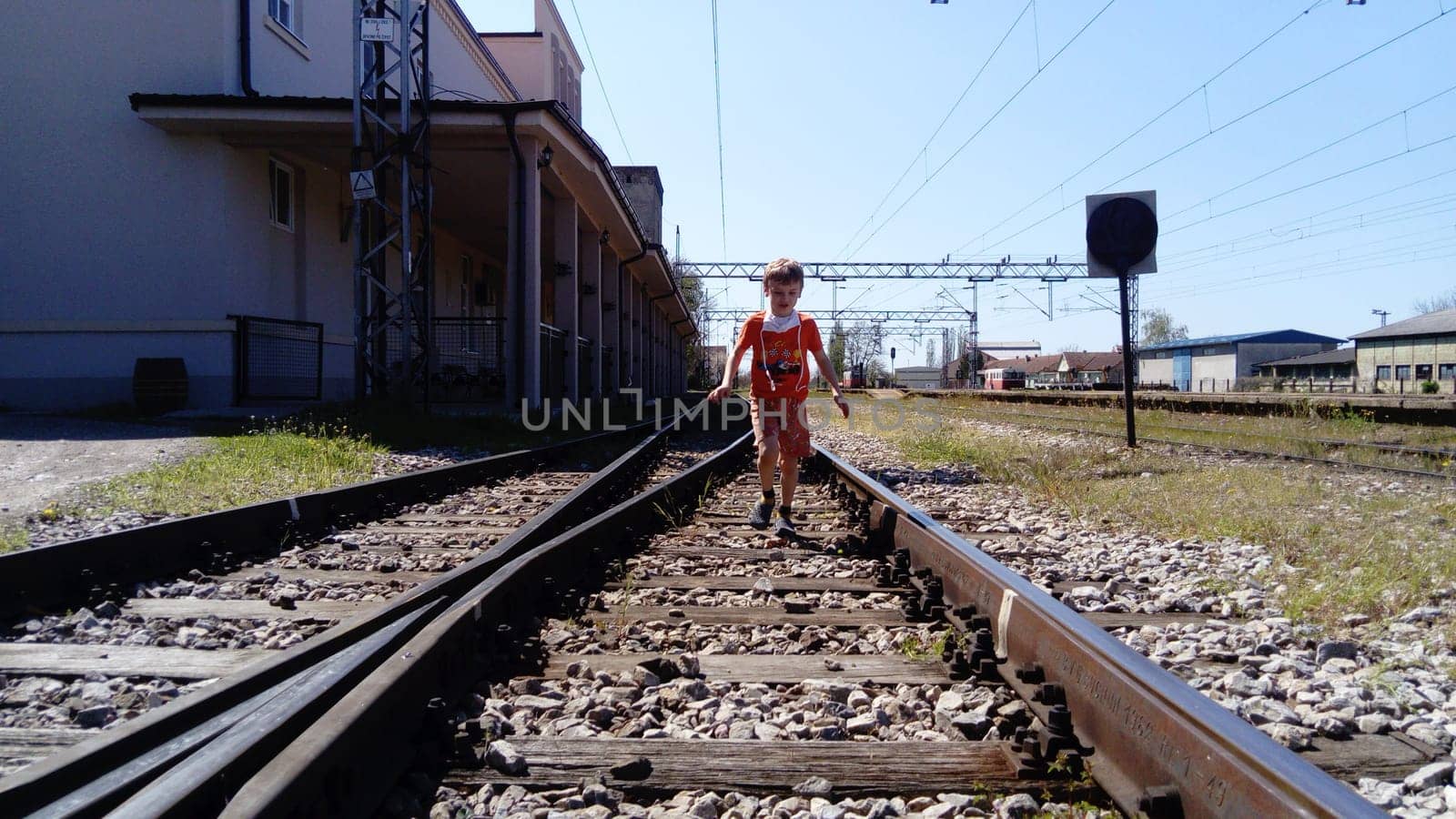 Sremska Mitrovica, Serbia, June 1, 2020. Boy with a protective mask runs on the railroad. Railroad tracks and station. Danger on the rails. Protection against respiratory viral diseases.