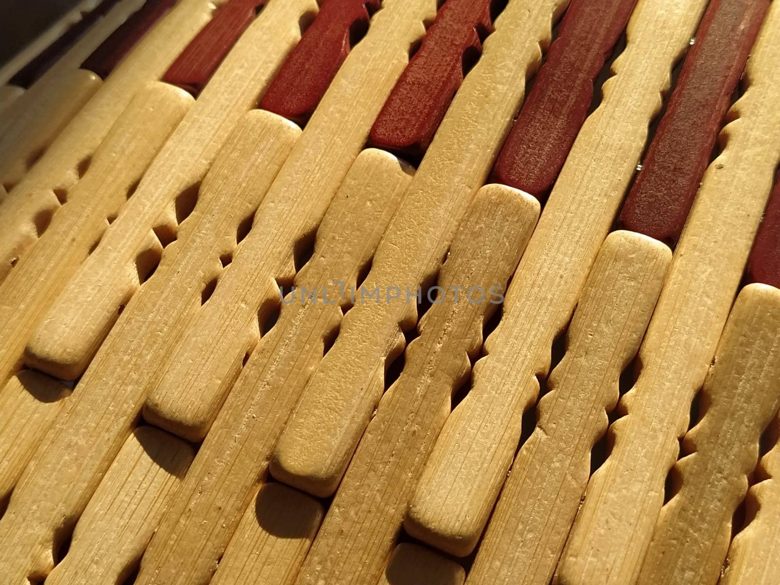 reed or wood mat. The rug is a mat under the hot. Knitted processed wood sticks with rounded edges. Close-up. Yellow, brown and beige colors. Side lighting. Traditional bamboo pad texture.