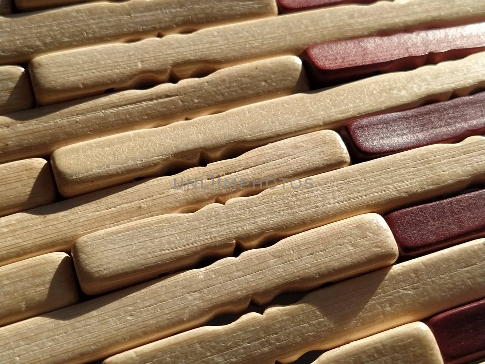 reed or wood mat. The rug is a mat under the hot. Knitted processed wood sticks with rounded edges. Close-up. Yellow, brown and beige colors. Side lighting. Traditional bamboo pad texture.