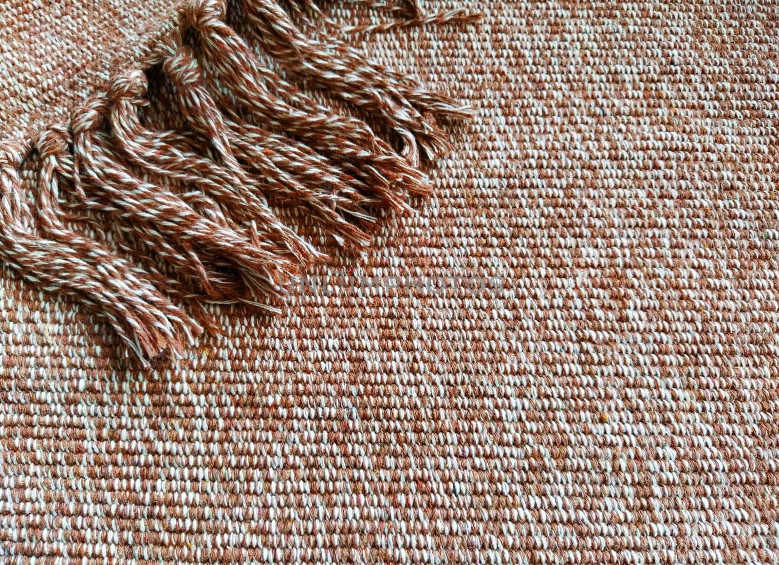 Woven fabric with tassels. Coarse weaving cotton. Floor mat. Beige, white and wrinkled threads in weaving. Woolen or acrylic material.