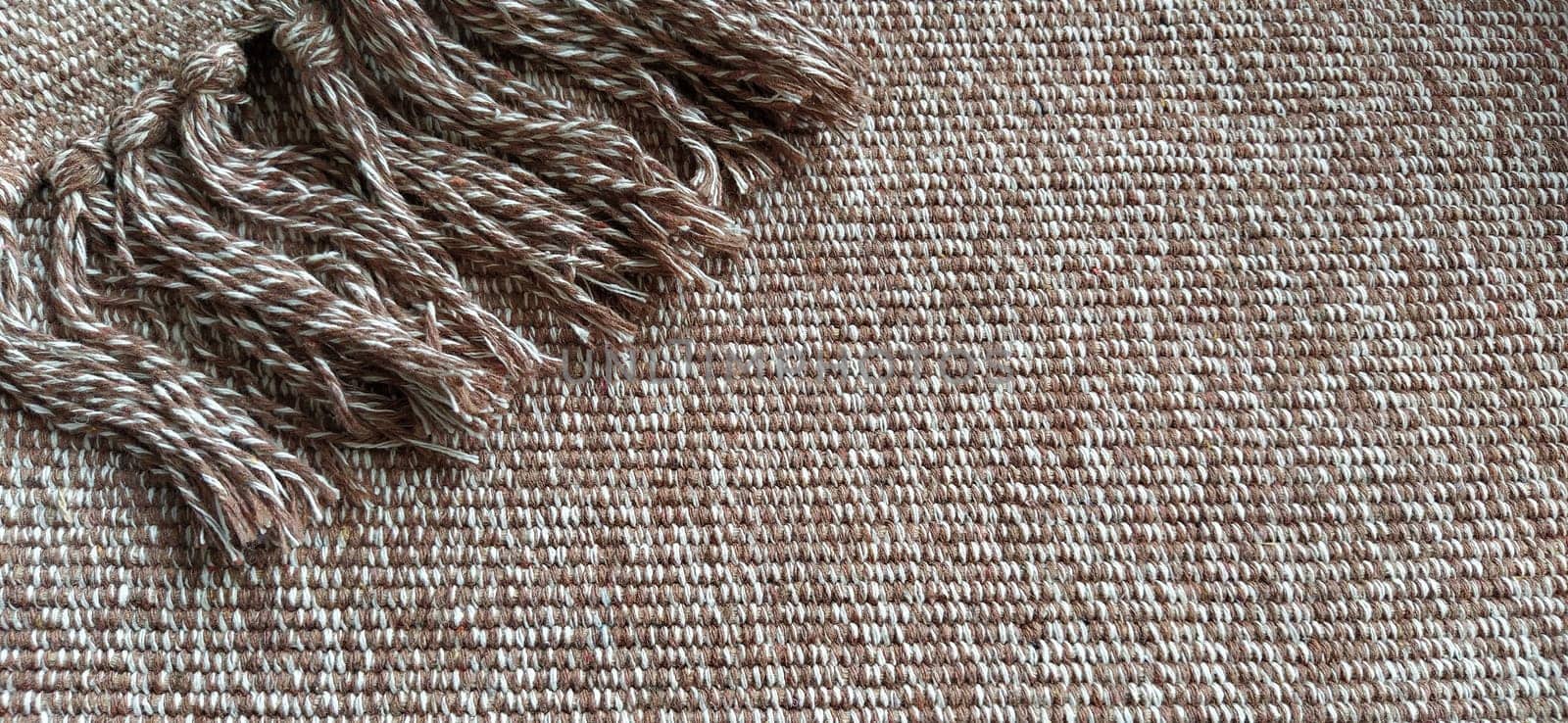 Woven fabric with tassels. Coarse weaving cotton. Floor mat. Beige, white and wrinkled threads in weaving. Woolen or acrylic material
