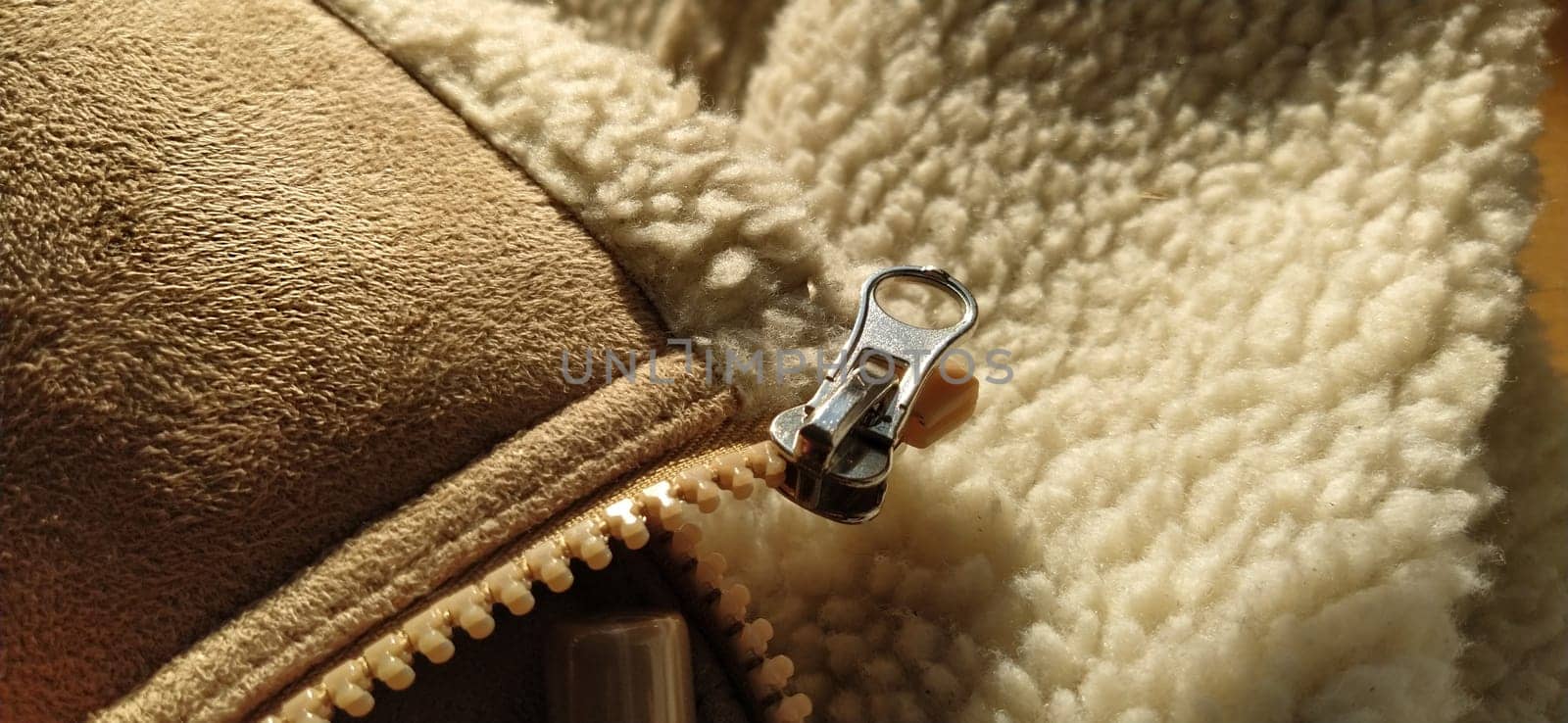 Zipper on suede sheepskin clothing. The metal element is the clasp. Light fur on the hem of a leather product. Close-up. Sewing supplies. Work of the cutter and seamstress