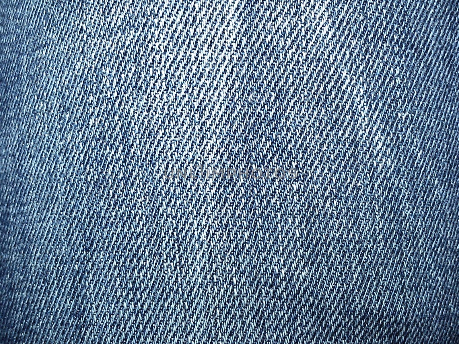 Blue denim. Texture of cotton coarse material. A fragment of a natural rag indigo. Vertical furrows, dark and light threads, individual stitches are noticeable. Crumpled spots on a piece of fabric.