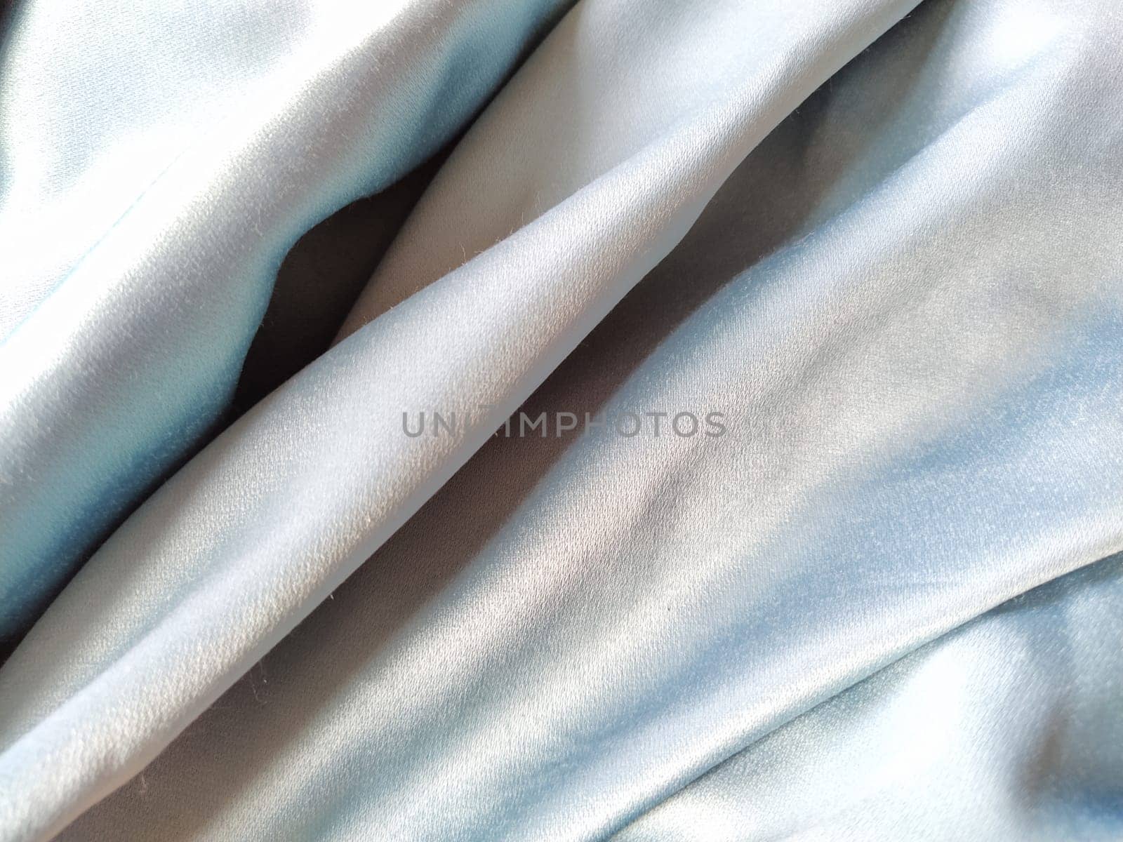Silky to the touch fabric of gray - blue color with a brilliant shimmer. Natural lighting, light and shadow. The material is casually folded. Polyester Textile.