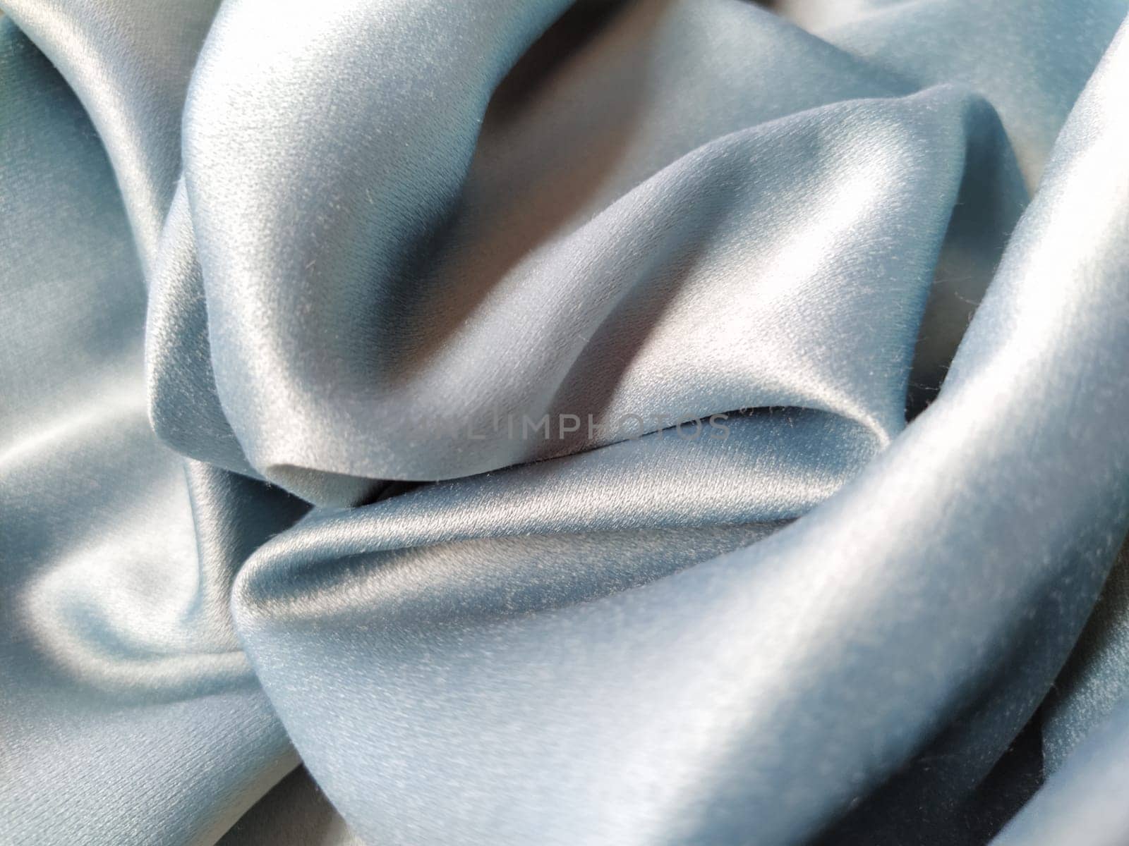 Silky to the touch fabric of gray - blue color with a brilliant shimmer. Natural lighting, light and shadow. The material is casually folded. Polyester Textile.