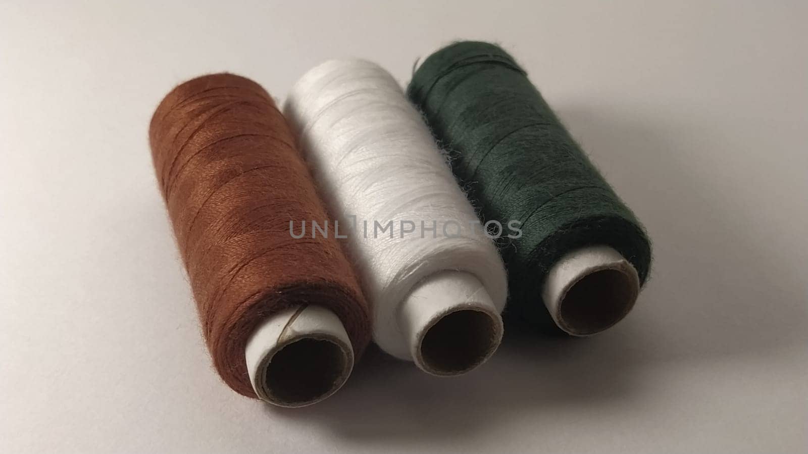 Bobbins and spools of thread of different colors - brown, white and green. Close-up. Natural light on the left side. Skeins of thread. Sewing supplies